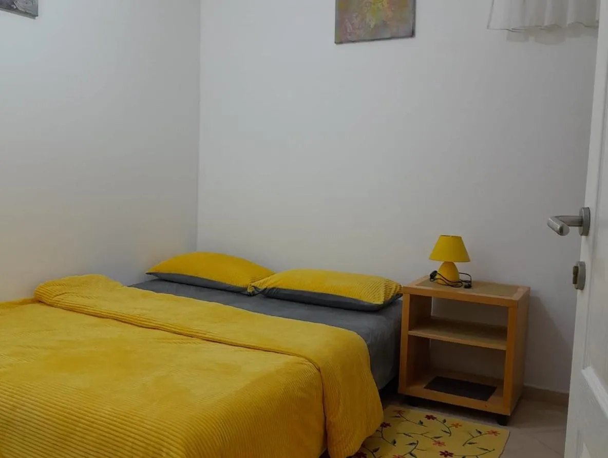 Manja spavaća soba sa žutom posteljinom i noćnim ormarićem